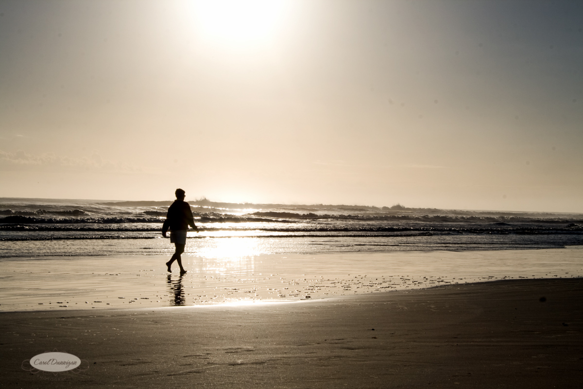 The sunrise is getting higher in the sky, as a lone person walks on Daytona Beach in Florida. You can see the ocean and waves in the background.