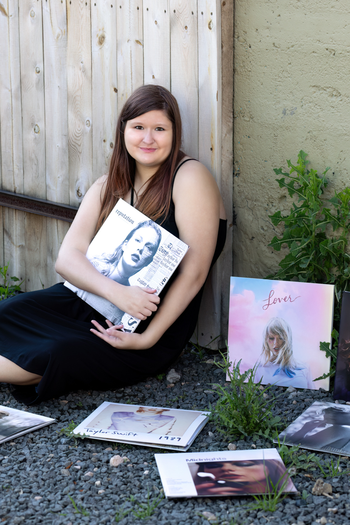 A high school senior is sitting on the ground with Taylor Swift albums laying all around her and she's holding one during her senior session in Fort Collins Colorado with Carol Dunnigan Photography.