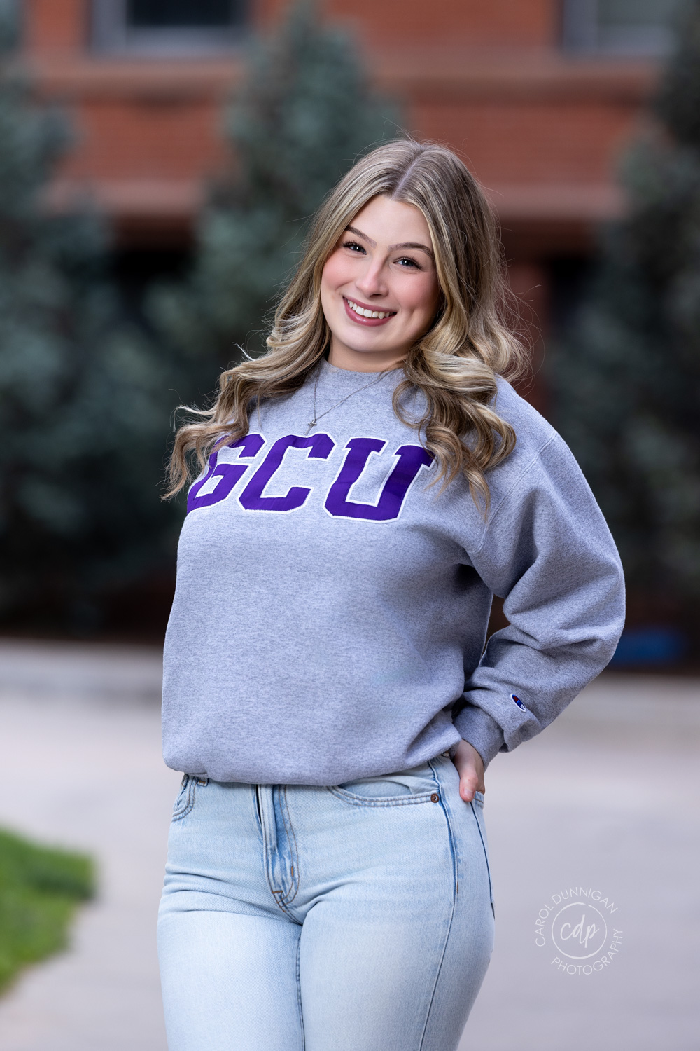 a high school graduate is standing smiling at the camera wearing her GCU sweatshirt for the college she is going to attend.