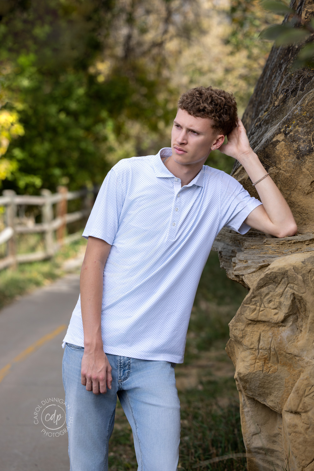 high school senior boy posing by a rock cliff with trees in the background in greeley colorado photographed by carol dunnigan photography