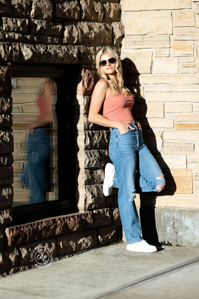 High School senior girl posing against a brick wall with sunglasses on during her senior session in Fort Collins by Carol Dunnigan Photography.
