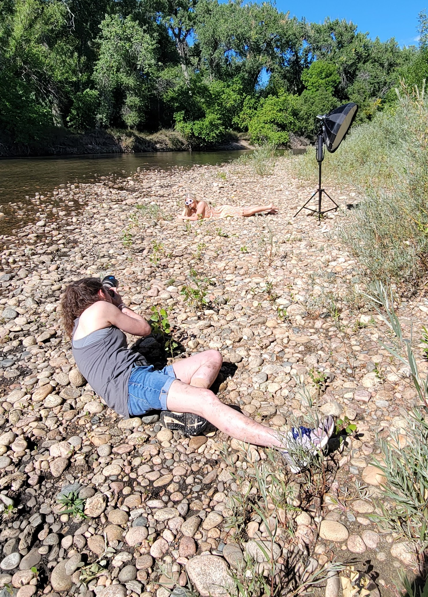 Behind the scenes showing the Carol Dunnigan Photography lying on a bed of river rock, photographing a high school senior girl who is also lying on the river rock in Fort Collins.