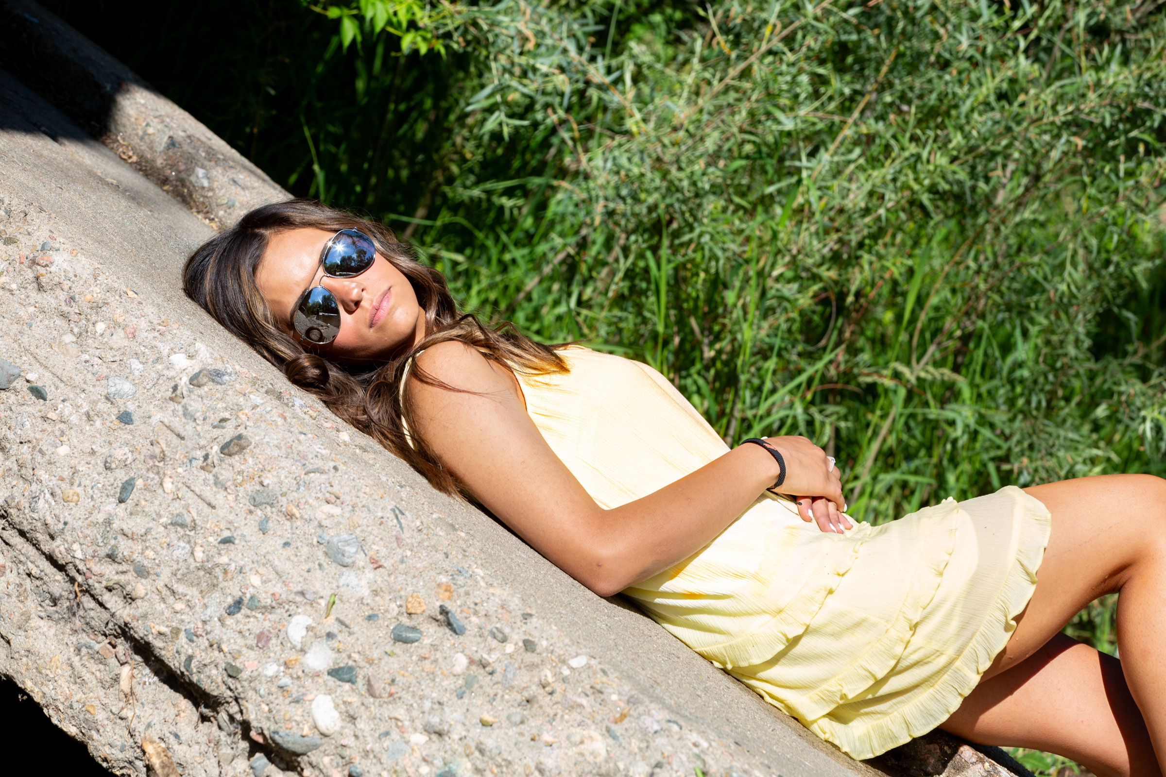 senior pictures with a high school girl lying on a vertical boulder in loveland colorado she's wearing a yellow dress and sunglasses by carol dunnigan photography