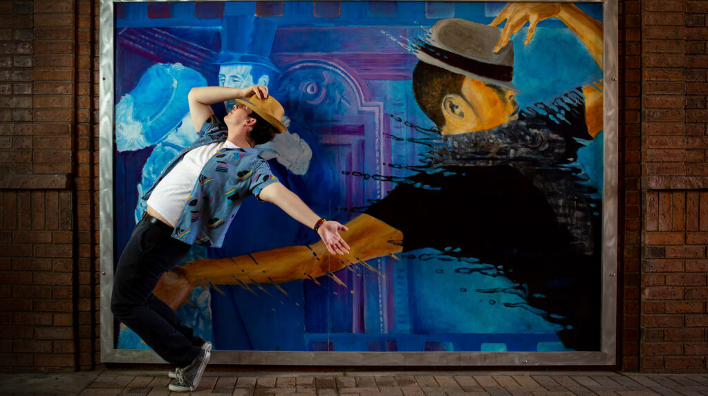 Creative urban senior pictures in downtown Greeley, Colorado with a senior guy and a mural. He's doing the same stand on toes and lean backward pose.