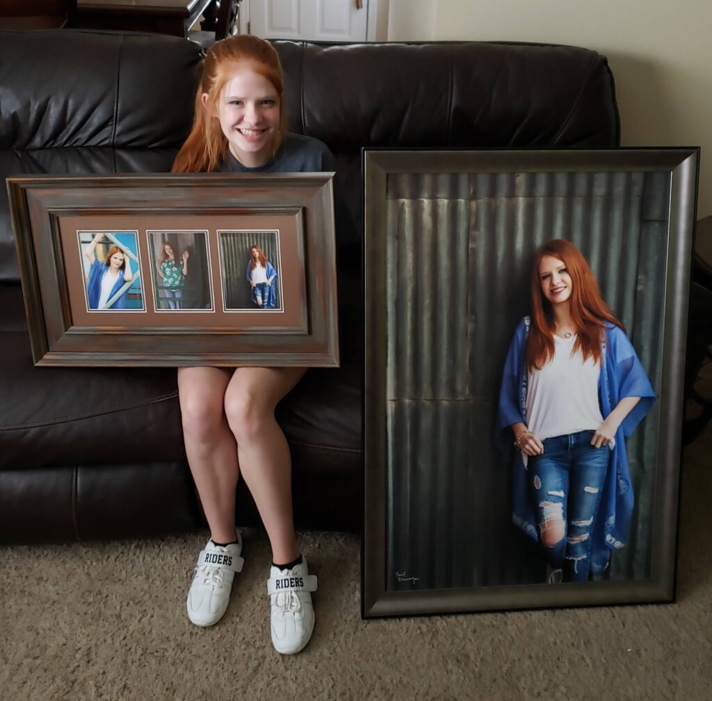 High school senior displaying framed wall art from her senior portrait session.