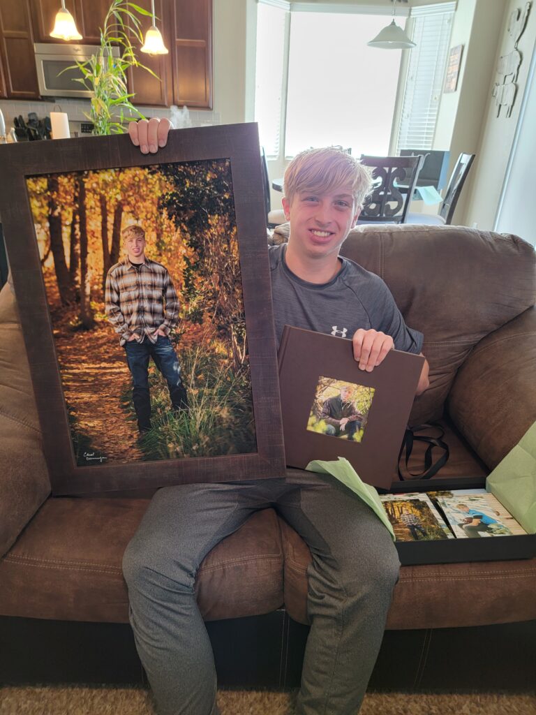 High school senior holding a framed portrait and custom album from his senior portrait session.