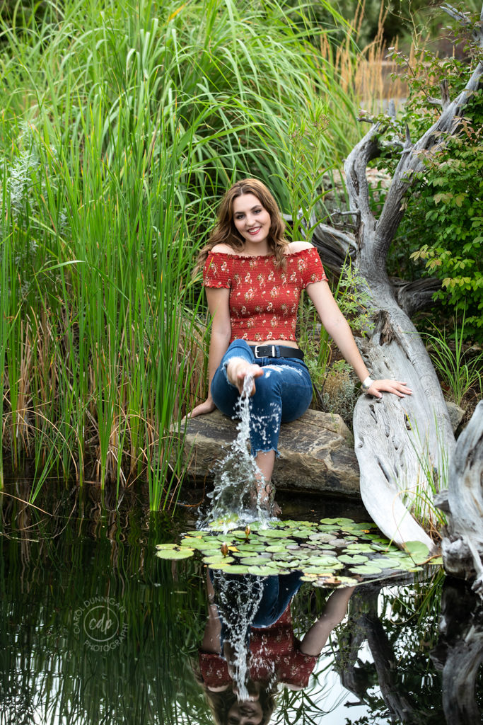 Delaney posing near the pond at the Rock Garden in Fort Collins during her senior portrait session, kicking the water up with her foot.