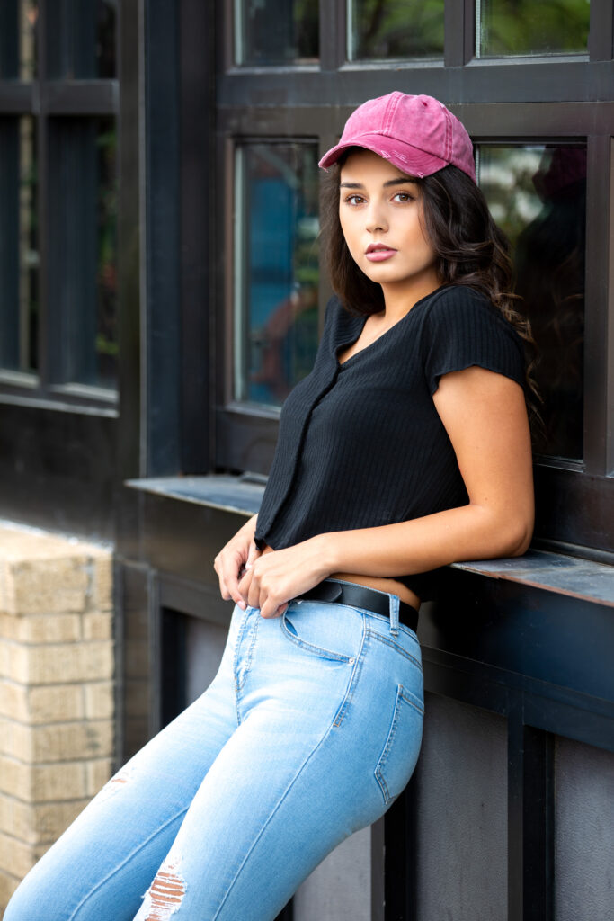 High school senior wearing a black top, jeans, and a pink baseball cap for downtown senior pictures in Fort Collins Colorado.