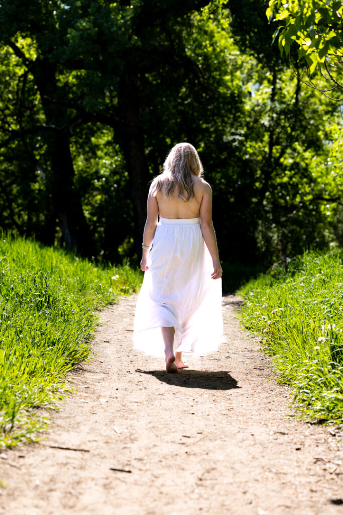 High school senior wearing a white dress walking barefoot on a wooded trail in Fort Collins Colorado.