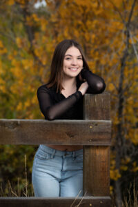 Senior Girl is leaning on a wood post smiling at the camera for senior pictures in Evans, Colorado.