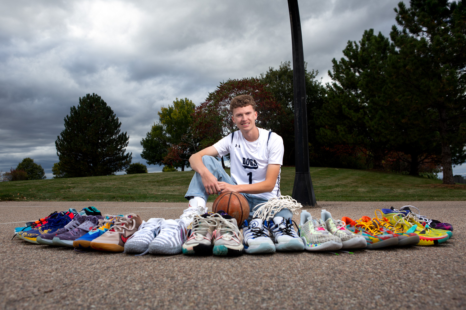 University High School basketball player during his senior session sitting on an outdoor basketball court with a ball and many pairs of gym shoes in front of him.