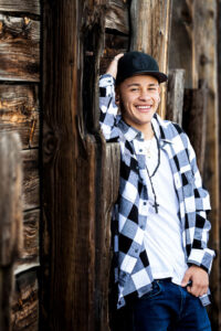 A high school guy is posing for his senior pictures against a wall of railroad ties during his senior session with Carol Dunnigan Photography in Greeley, Colorado.