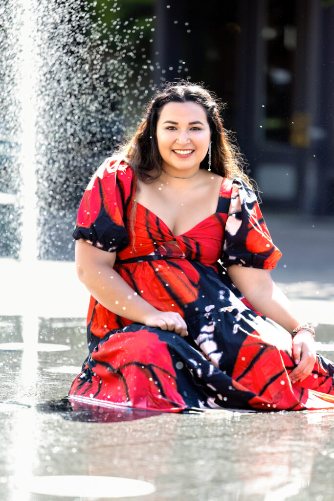 High school senior wearing a colorful dress sitting in a Fort Collins Colorado fountain for senior portraits.