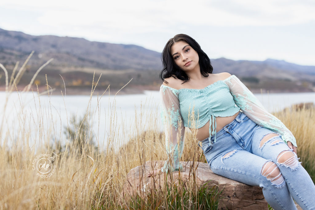 Jayna posing in the grasses with Horsetooth Reservoir and the mountains behind her during her senior portrait session