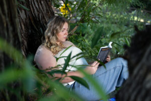 A high school senior girl is sitting inside a tree, pretending to read one of her favorite books during her senior session with Carol Dunnigan Photography in Fort Collins Colorado.