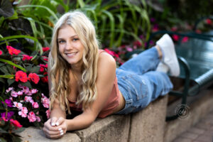 A girl is posing by lying in Fort Collins Colorado on a cement ledge with flowers in it for her senior pictures.