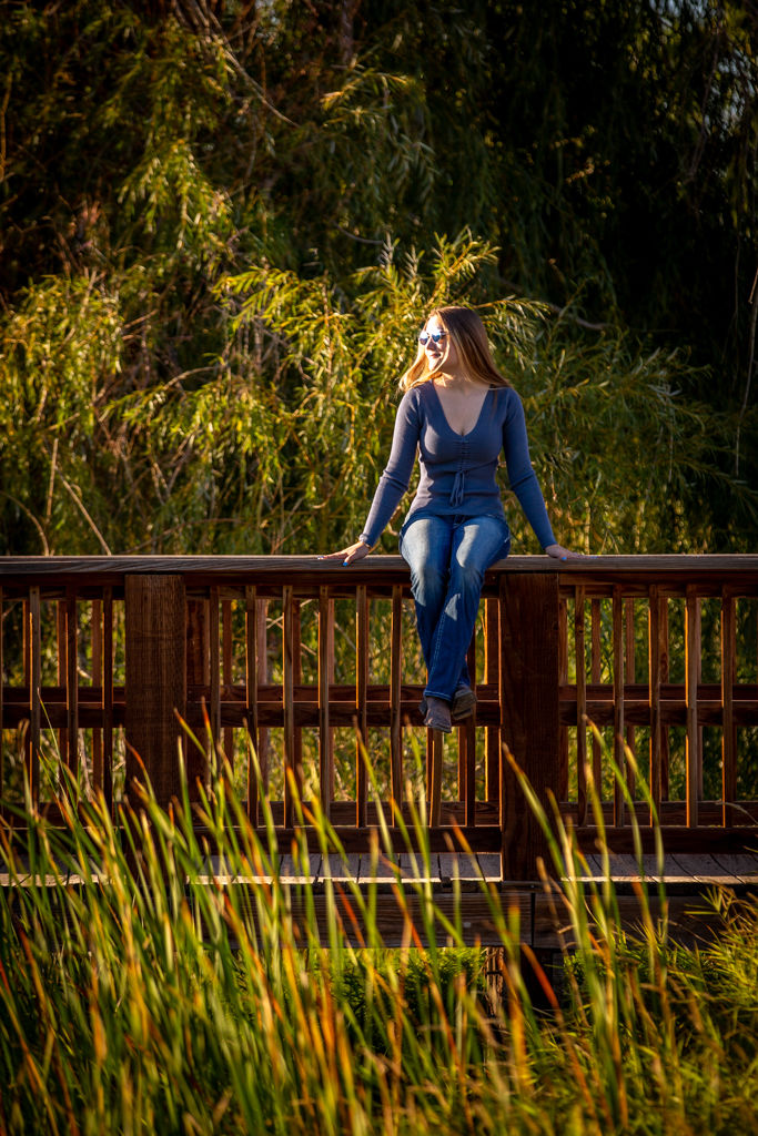 High school senior in Greeley Colorado wearing a blue long-sleeve top and jeans sitting on a wooden bridge.