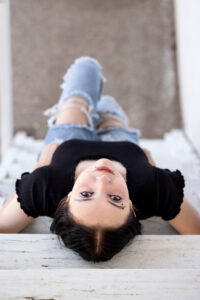 A senior girl is posing on a staircase, looking up at Carol Dunnigan who is photographing her senior pictures in Ault, Colorado.