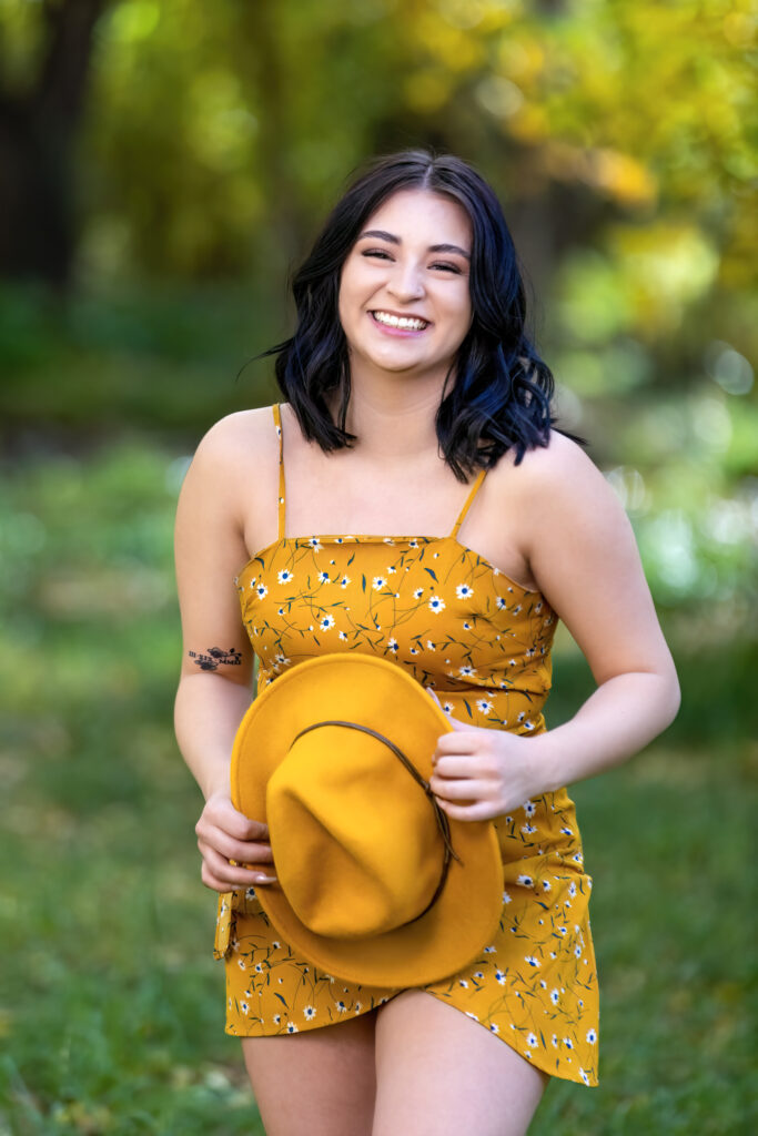 High school senior wearing a yellow floral dress and holding a matching hat in Loveland Colorado.