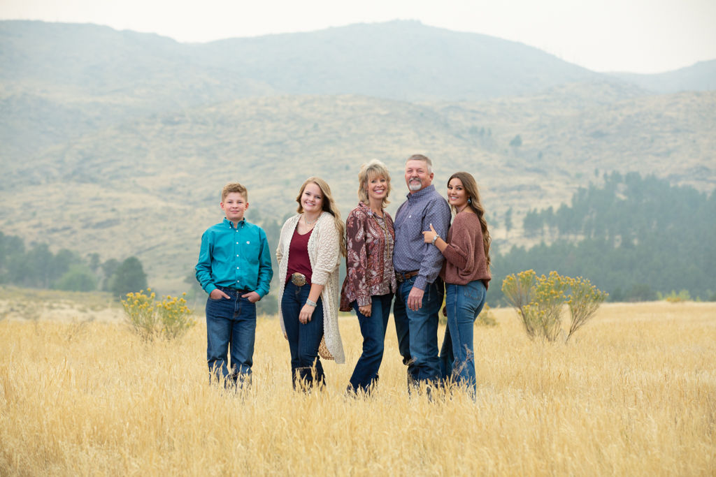 Family of 5 standing in a field of short wheat grass with mountains behind them and a smoky atmosphere from fires nearby in Loveland, Colorado.