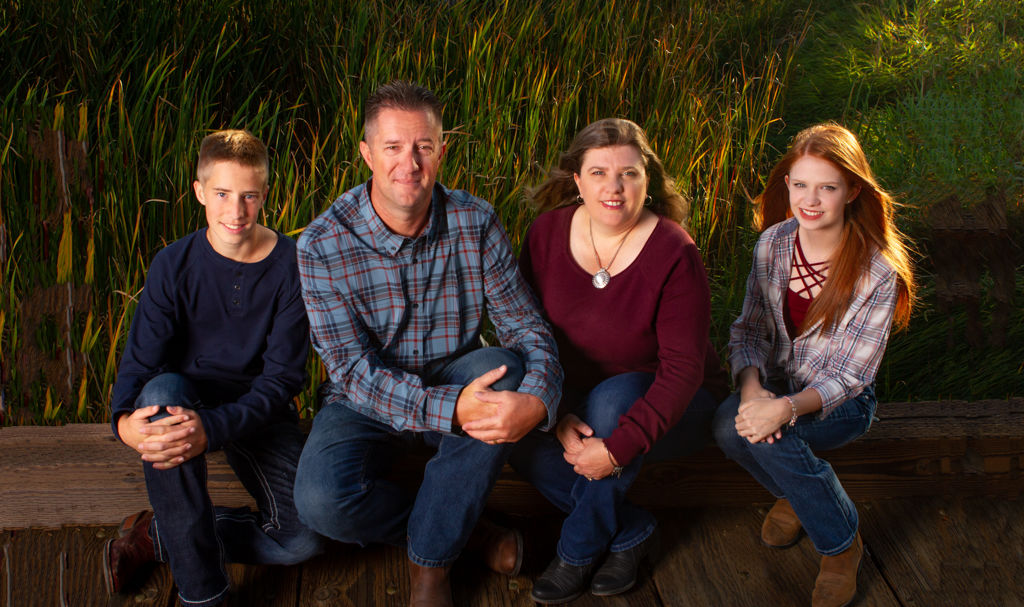 Family of 4 sitting on a railroad tie bridge in the evening sunlight.