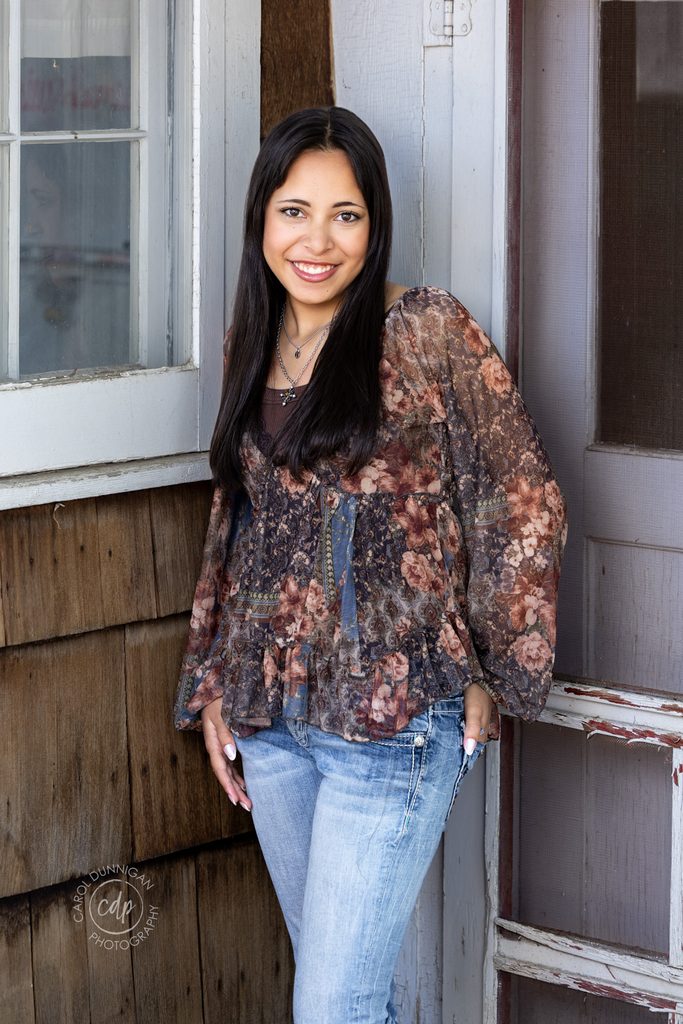 High school senior in a floral blouse posing on a porch during her Greeley, Colorado senior portrait session