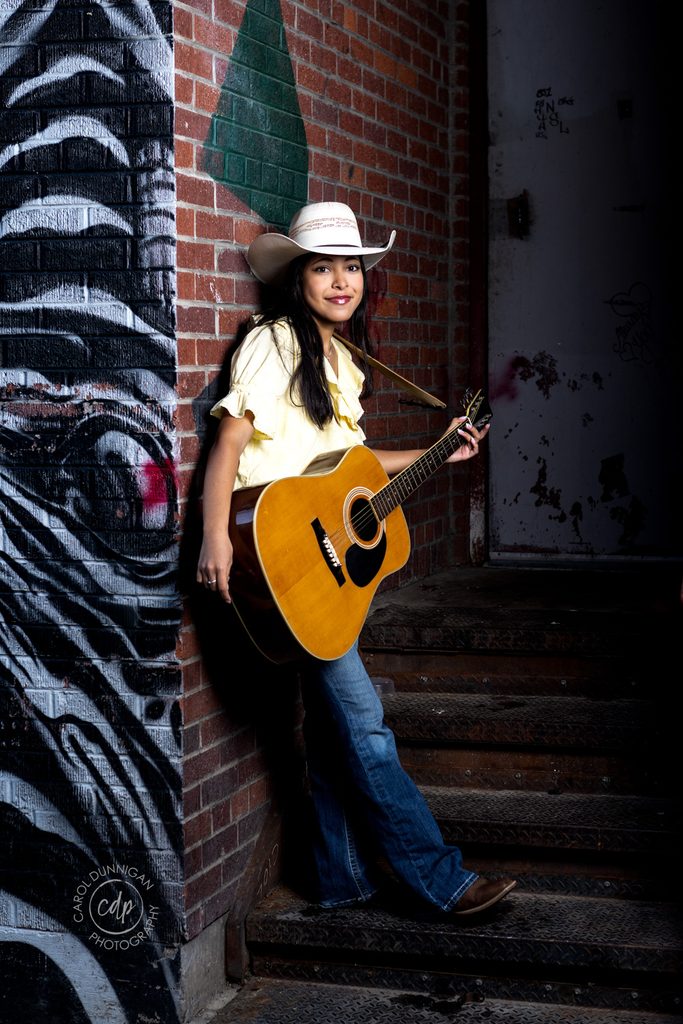 High school senior posing with a guitar and cowboy hat during her Greeley, Colorado senior portrait session