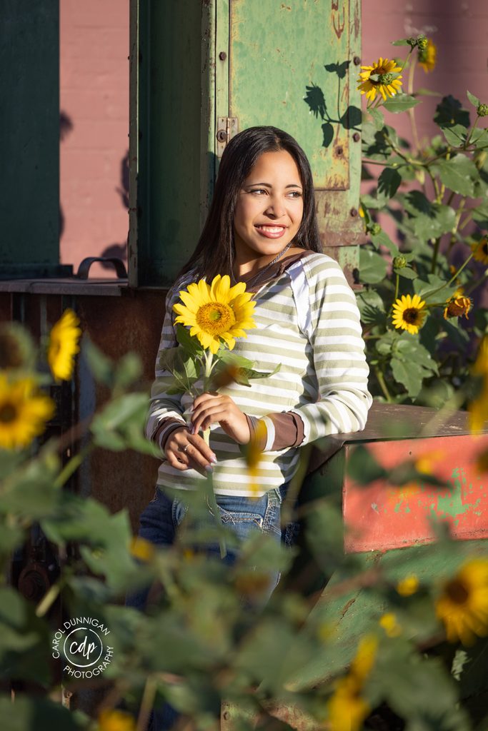 High school senior holding a sunflower during her colorful Greeley, Colorado senior portrait session