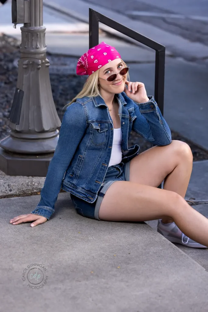 Juliaunna wearing sunglasses and sitting on a sidewalk during her downtown Loveland senior pictures