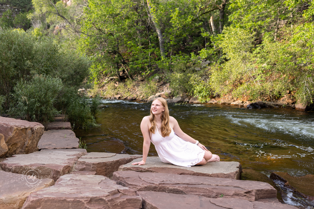 : High school senior sitting beside the river in Lyons, Colorado during her senior portrait session