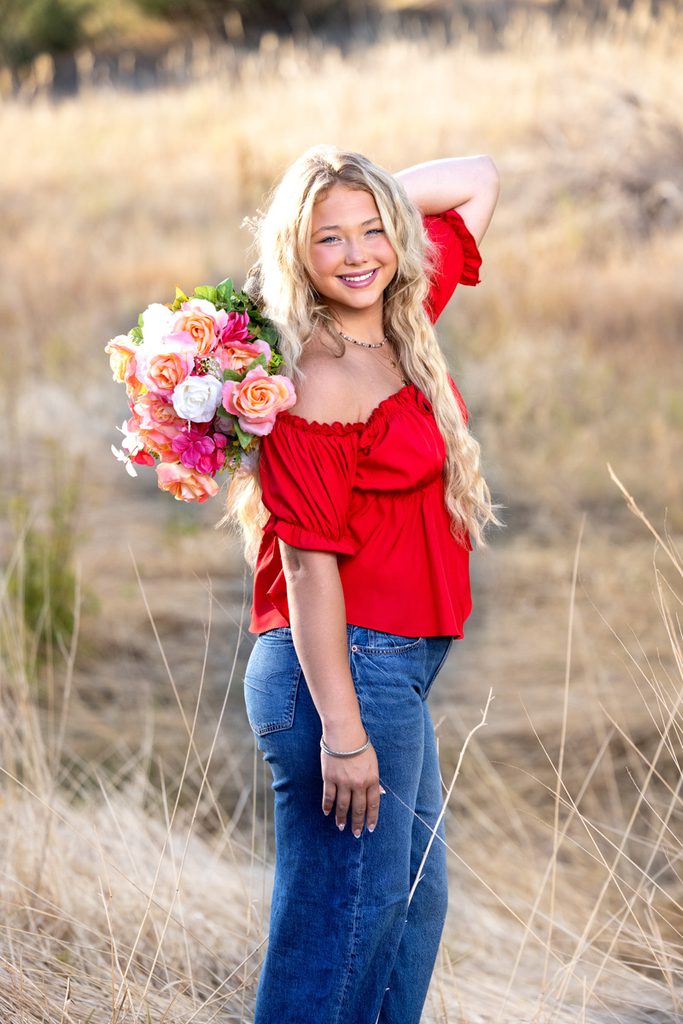 Senior girl in a red top holding a bouquet of flowers during her yearbook portrait session in West Loveland.