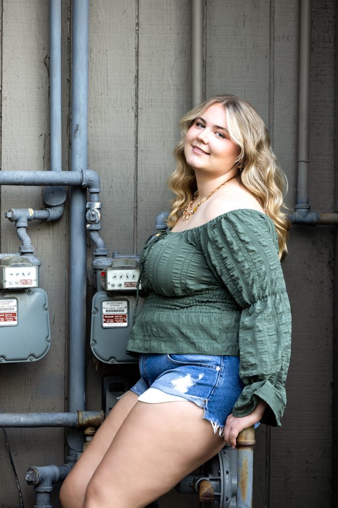Senior girl in a green top and denim shorts posing for a yearbook portrait in Old Town Fort Collins.